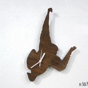 May include: A wooden clock shaped like a person in a skydiving pose. The clock has white hands and is mounted on a white wall. The text "By Sol Pixie Dust" is visible in the bottom right corner of the image.