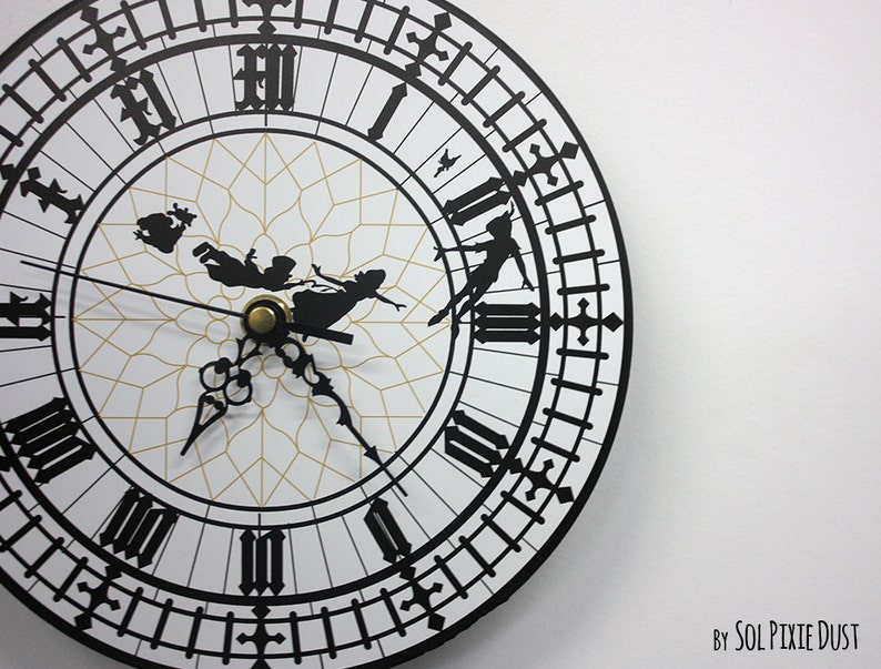 May include: A black and white clock face with Roman numerals and a silhouette of Peter Pan and Tinkerbell flying. The clock face is surrounded by a black border with a repeating pattern of black lines and crosses. The text "By SOL PIXIE DUST" is visible in the bottom right corner of the image.