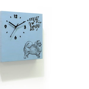 May include: A light blue square wooden clock with black hands and black numbers. The clock face has a black and white illustration of a dog and the text "my love" with a heart and arrow.