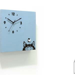 May include: A light blue square wooden cuckoo clock with a black cat peeking out from behind a small white door. The clock face has black hands and black numbers.