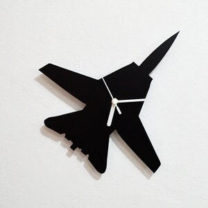 May include: Black wall clock shaped like a fighter jet with white hands.