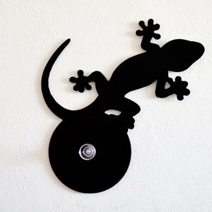 May include: Black metal gecko wall hook with a round base. The gecko is curled around the base and has a textured surface.