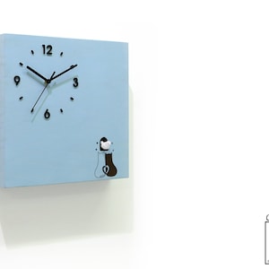 May include: A light blue square clock with black hands and numbers. The clock has a black and white illustration of two people holding hands. The clock is labeled "Cuckoo Clocks Time Box by Sol Pixie Dust".