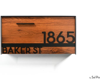 Puede incluir: Un buzón rectangular de pared con un panel frontal de veta de madera y un marco de metal negro. El buzón muestra el número 1865 y el texto BAKER ST en letras negras en negrita, junto con un asa horizontal negra y delgada.