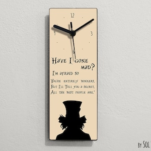 Puede incluir: Un reloj de color crema con agujas negras y una silueta negra del Sombrerero Loco de Alicia en el Pa&iacute;s de las Maravillas. La esfera del reloj tiene la cita "Have I gone mad? I'm afraid so. You're entirely bonkers. But I'll tell you a secret. All the best people are."