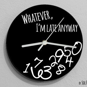 Pode incluir: Um relógio redondo preto com números e ponteiros brancos. O mostrador do relógio tem o texto "Whatever, I'm late anyway" escrito nele. O relógio é feito por Sol Pixie Dust.