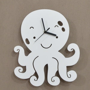 Op de afbeelding: Witte octopusvormige wandklok met zwarte wijzers en een glimlachend gezicht. De klok heeft een eenvoudig ontwerp met een ronde wijzerplaat en acht tentakels.
