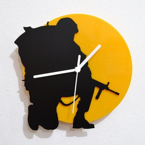 May include: A black silhouette of a soldier holding a rifle is cut out of a yellow circular clock face.