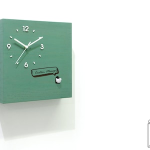 May include: A green square wooden cuckoo clock with white hands and numbers. The clock has a small white bird that pops out of the front. The clock face also has a speech bubble that says "Custom Message!"