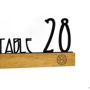 Puede incluir: Número de mesa negro con el texto "TABLE 20" sobre una base de madera con un pequeño logotipo.