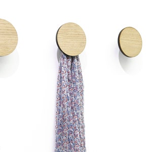 May include: Three round wooden wall hooks with a black edge. A scarf is hanging from the middle hook.