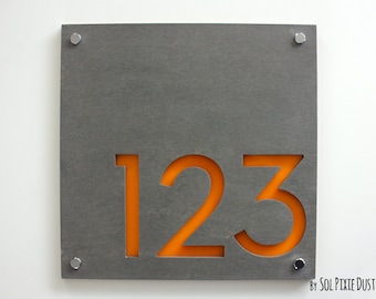 Puede incluir: Un letrero de número de casa de metal gris con el número 123 recortado y relleno de acrílico naranja.