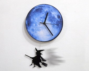 Peut inclure: Une horloge en forme de lune bleue avec une silhouette noire de sorcière volant sur un balai suspendue en dessous.