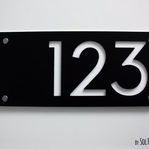 May include: Black rectangular house number sign with white cutout numbers 123. The sign has three silver screws on each side.