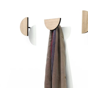 May include: Three wooden wall hooks shaped like half circles. The hooks are mounted on a white wall. One hook has a scarf hanging from it.