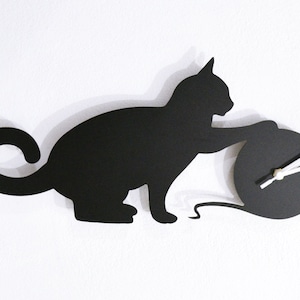 Könnte beinhalten: Schwarze Silhouette einer Katze, die mit einem Wollknäuel spielt, das gleichzeitig ein Zifferblatt mit weißen Zeigern ist.