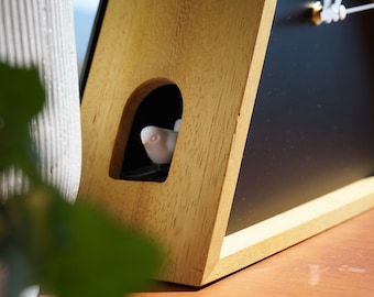 May include: A wooden clock with a black face and a small white bird figurine peeking out of a cutout in the wood. The clock is on a wooden surface.