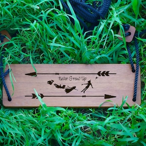May include: Wooden swing set with a brown wooden seat and black ropes. The seat has the words "Never Grow Up" and a silhouette of Peter Pan and the Lost Boys.