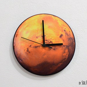Può includere: Un orologio rotondo con quadrante e lancette nere. Il quadrante dell'orologio presenta un'immagine dettagliata del pianeta Marte. Il testo "By SOL PIXIE DUST" è visibile nella parte inferiore dell'immagine.