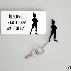 Könnte beinhalten: Ein schwarz-weißer Schlüsselanhänger mit einer Silhouette von Peter Pan und dem Zitat "Alles, was du brauchst, ist Glaube - Vertrauen und Feenstaub".