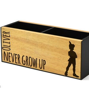 May include: Wooden desk organiser with two compartments. The organiser is decorated with a silhouette of Peter Pan and the text "OLIVER NEVER GROW UP".