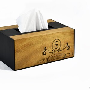 May include: A wooden tissue box cover with a black trim. The cover is personalized with the initial "S" in a circle, the names "Melissa & Oliver", and the date "Est. 2009".