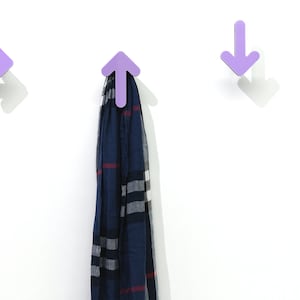 May include: Three purple arrow-shaped hooks mounted on a white wall. The middle hook has a blue and white plaid scarf hanging from it. The text "By Sol Pixie Dust" is visible at the bottom of the image.