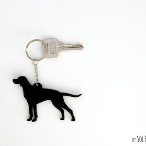 Peut inclure: Silhouette noire d'un chien sur un porte-clés argenté avec une clé attachée. Le porte-clés est marqué "By SOL PIXIE DUST".