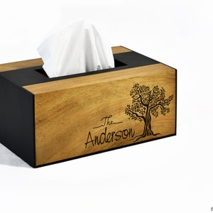 Może przedstawiać: Drewniana pokrywa na pudełko na chusteczki z czarną obwódką. Z przodu znajduje się laserowo grawerowany wzór drzewa z tekstem "The Anderson" poniżej.
