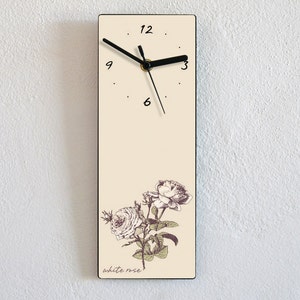 May include: A beige rectangular clock with black hands and black Roman numeral markings. The clock face has a white rose illustration and the text "white rose" at the bottom.