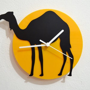May include: A yellow circular clock with a black silhouette of a camel. The clock hands are white.