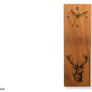 May include: A wooden wall clock with a black clock face and black hands. The clock face has Roman numerals for the hours. The clock is decorated with a laser-engraved image of a stag's head with antlers. The clock is made by Sol Pixie Dust.