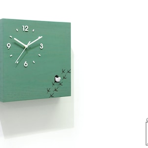 May include: A green wooden cuckoo clock with a white bird and black bird tracks. The clock face has white numbers and hands. The clock is labeled "Cuckoo Clocks Time Box by Sol Pixie Dust".