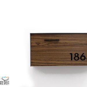 May include: A wooden mailbox with a black metal frame and a black metal handle. The mailbox has the number 1865 printed on it.