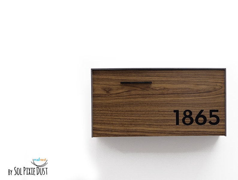 May include: A wooden mailbox with a black metal frame and a black metal handle. The mailbox has the number 1865 printed on it.