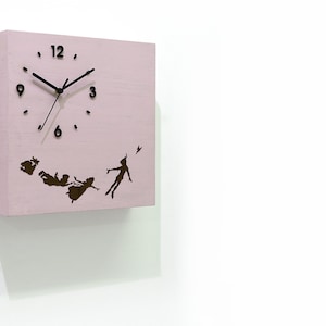 May include: A pink square wooden clock with black hands and numbers. The clock features a silhouette of Peter Pan and the Darling children flying.