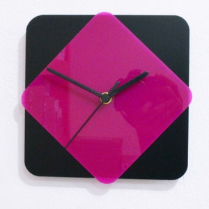 Puede incluir: Un reloj cuadrado negro con una cara de diamante de color rosa brillante y manecillas negras.
