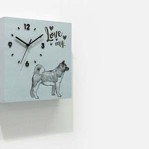 Puede incluir: Un reloj cuadrado de madera azul claro con agujas negras y números negros. La esfera del reloj tiene una ilustración en blanco y negro de un perro Akita y el texto "Love my" con corazones.