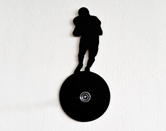 May include: Black silhouette of a football player standing on a round black base with a hook. The player is holding a football in their left hand.