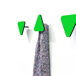 Puede incluir: Tres ganchos de pared de forma triangular verde con bordes negros. Los ganchos están montados en una pared blanca. Una bufanda estampada cuelga de uno de los ganchos.