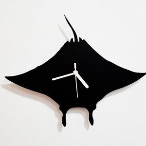 Puede incluir: Reloj de pared negro en forma de manta raya con agujas blancas.