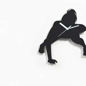 May include: Black silhouette wall clock shaped like a person doing a handstand. The clock has white hands.