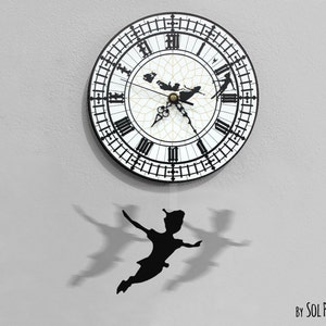 May include: A black and white clock face with Roman numerals and a silhouette of Peter Pan flying. The clock is hanging from a white wall and has a black silhouette of Peter Pan hanging from the bottom.