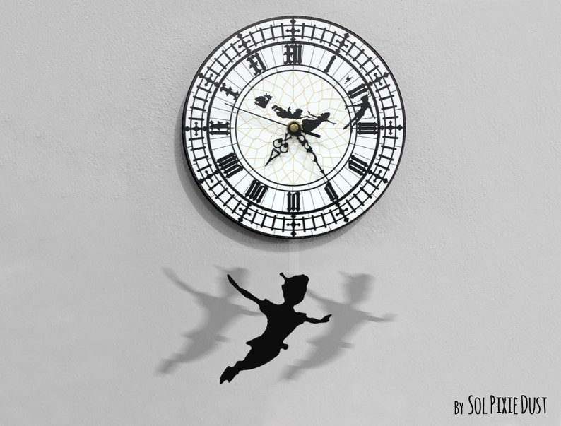 May include: A black and white clock face with Roman numerals and a silhouette of Peter Pan flying. The clock is hanging from a white wall and has a black silhouette of Peter Pan hanging from the bottom.