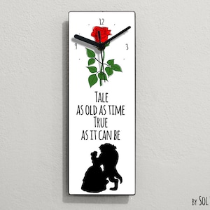May include: A white clock with a black clock face and black hands. The clock face has black Roman numerals. A red rose with green leaves is on the clock face. The clock has a white background with black text that reads "TALE AS OLD AS TIME TRUE AS IT CAN BE". The clock is framed in black. Below the clock is the text "BY SOL PIXIE DUST".