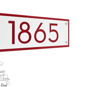 Könnte beinhalten: Rotes und weißes Hausnummernschild mit der Nummer 1865 in Rot. Das Schild ist aus Acryl und hat ein modernes Design.