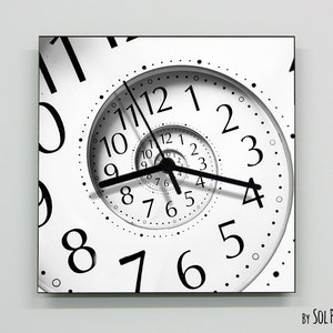 May include: A black and white clock with a spiral design. The clock face has black numbers and hands. The clock is framed in a black frame.