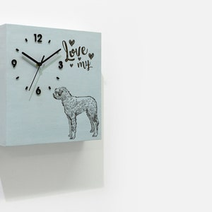 Puede incluir: Un reloj cuadrado de madera azul claro con agujas negras y números negros. La esfera del reloj tiene una ilustración en blanco y negro de un perro y el texto "Love my" con corazones.