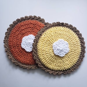 May include: Two crocheted pot holders, one orange and one yellow, with a white crocheted center. The pot holders have a brown crocheted border.