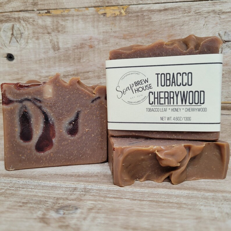 Peut inclure: Un savon brun avec des tourbillons rouges. Le savon est &eacute;tiquet&eacute; "Tobacco Cherrywood" avec le texte "Soap Brew House" et "Tobacco Leaf * Honey * Cherrywood" et "Net Wt. 4.6oz/130g".